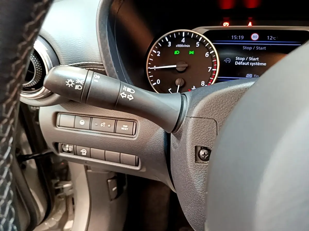 Détail du tableau de bord et commodo gauche du Nissan Juke 2022 essence, affichage multifonctions et compte-tours visibles.