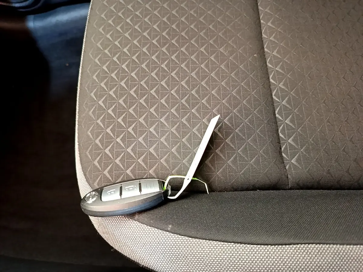 Clé de voiture Nissan Juke posée sur la banquette arrière en tissu gris foncé avec motif géométrique.