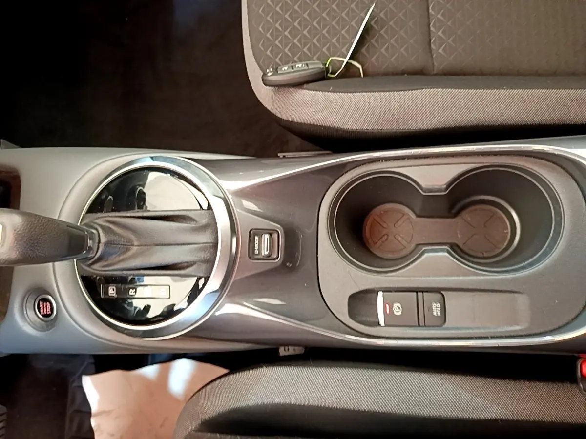 Vue plongeante sur la console centrale noire du Nissan Juke gris clair, avec levier de vitesse automatique et porte-gobelets.
