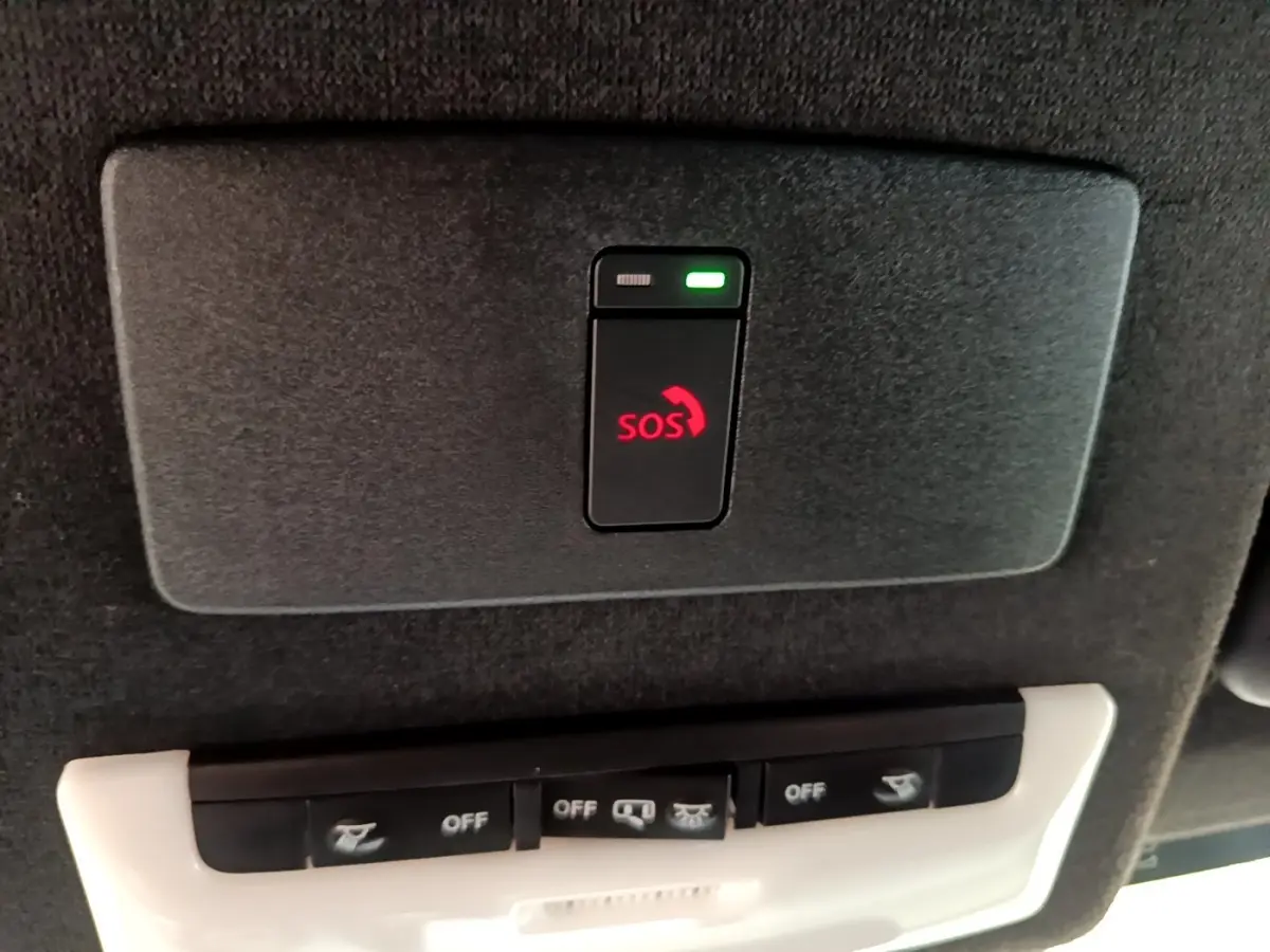 Gros plan sur le bouton SOS rouge et les commandes d’éclairage intégrées au plafond intérieur du Nissan Juke gris clair.