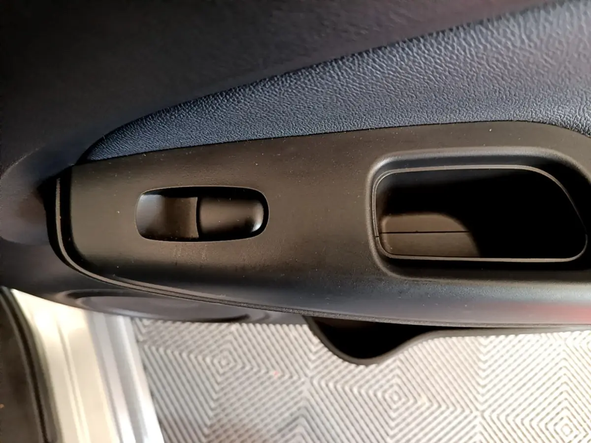 Gros plan sur la poignée intérieure noire de porte avant d'un Nissan Juke gris clair, vue côté conducteur.