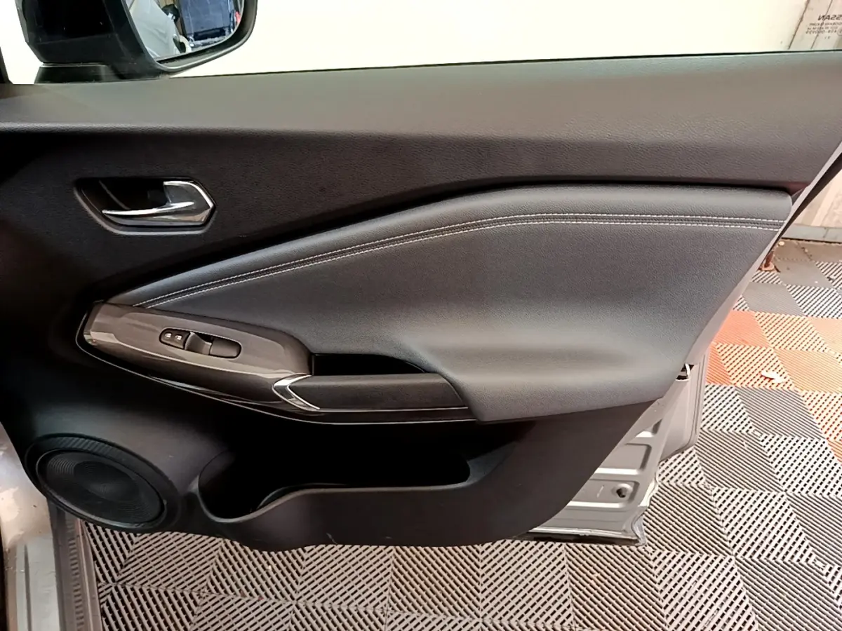 Vue intérieure côté gauche de la porte avant d’un Nissan Juke gris clair, avec commandes électriques et haut-parleur intégré.