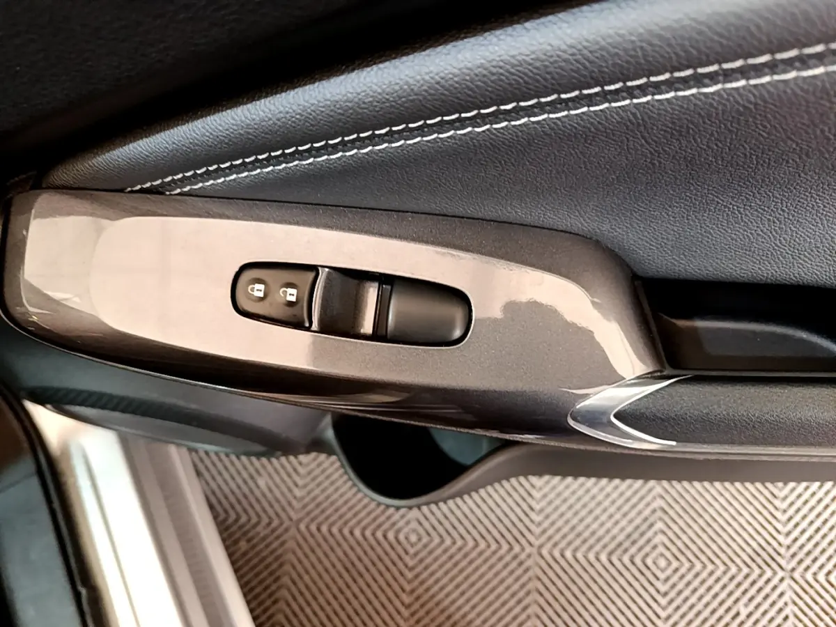 Gros plan sur la commande de verrouillage des portes côté conducteur du Nissan Juke gris clair, avec garniture cuir noire.