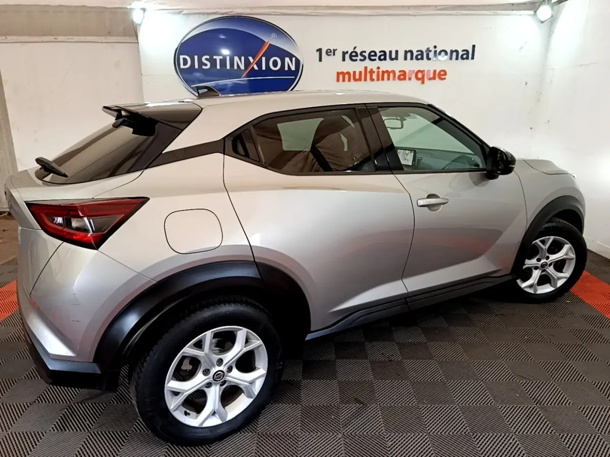 Nissan Juke gris clair vu de profil droit, avec toit noir et jantes alliage cinq branches, en intérieur showroom.