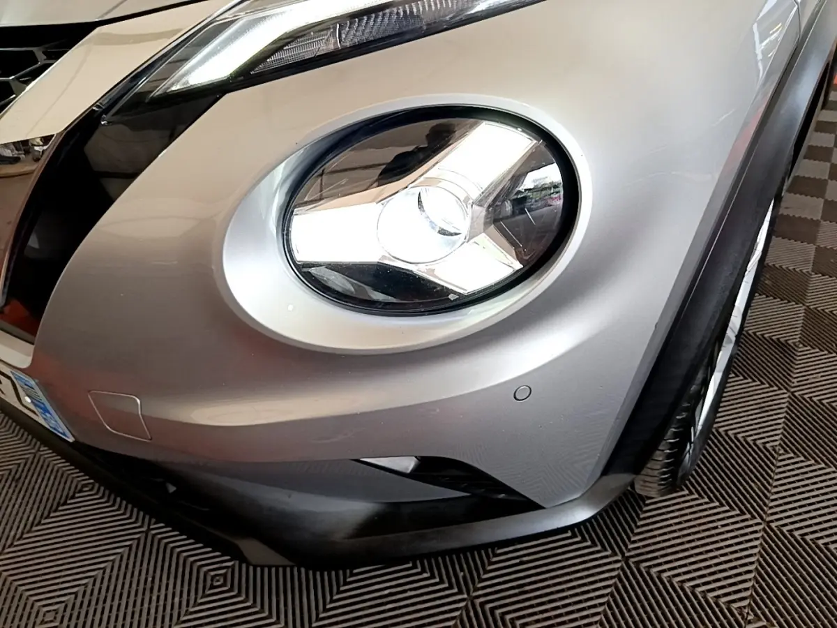 Gros plan sur le phare avant droit du Nissan Juke gris clair, mettant en valeur le design arrondi et le pare-chocs.