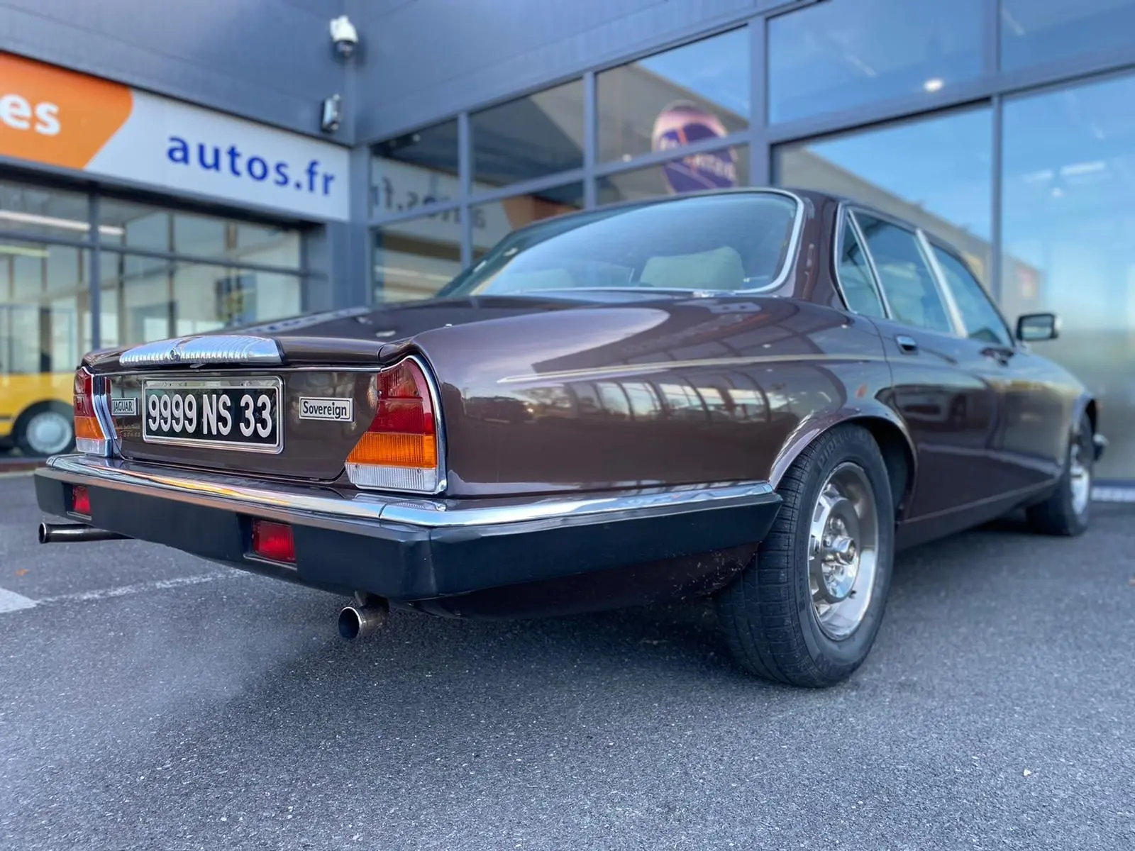 Vue 3/4 arrière droite d'une Jaguar XJ6 Série 3 4.2 Sovereign marron de 1985 avec plaques françaises et feux caractéristiques.