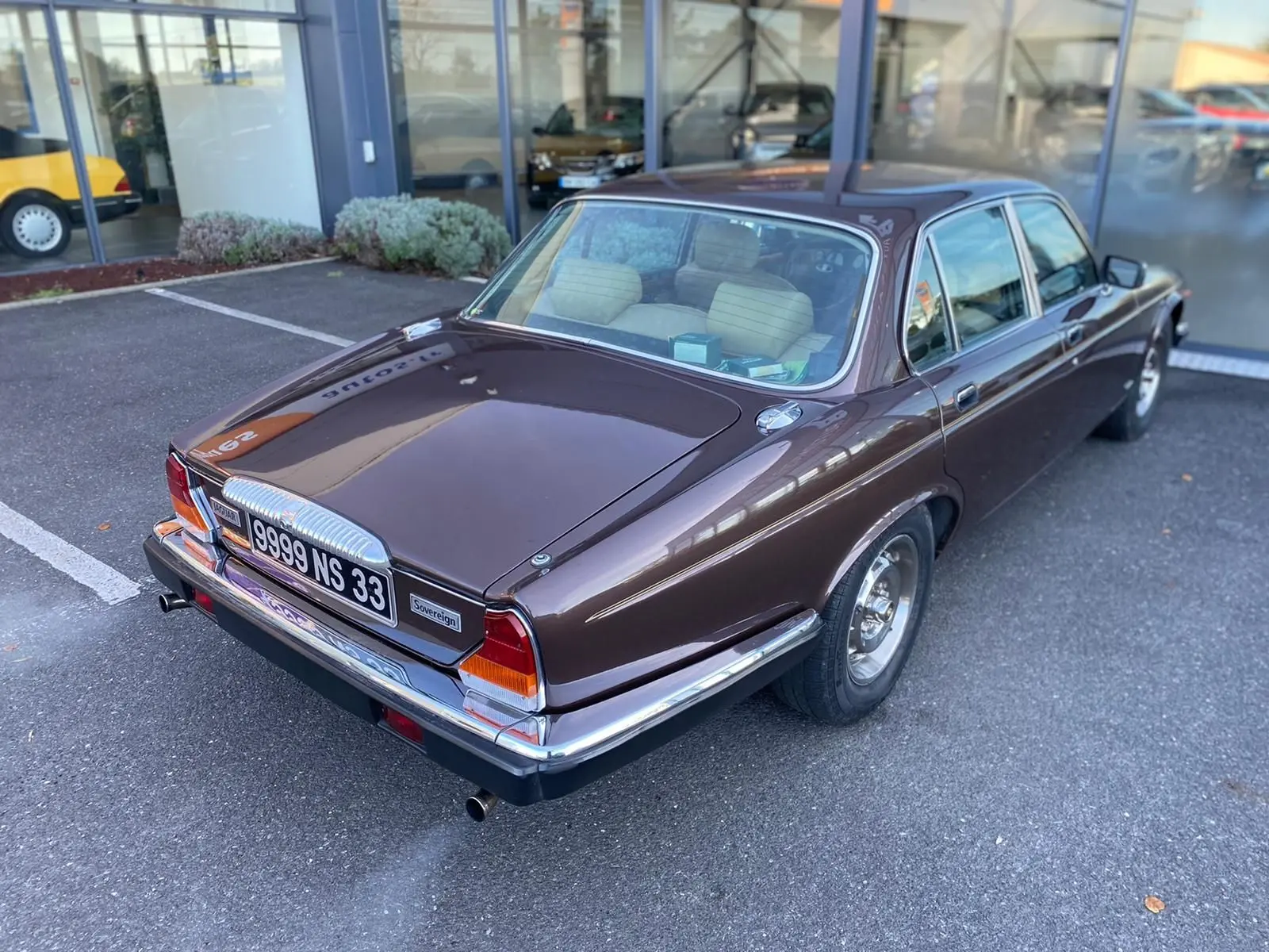 Vue 3/4 arrière droite d'une Jaguar XJ6 Série 3 4.2 Sovereign marron de 1985 avec détails chromés et intérieur clair visible.