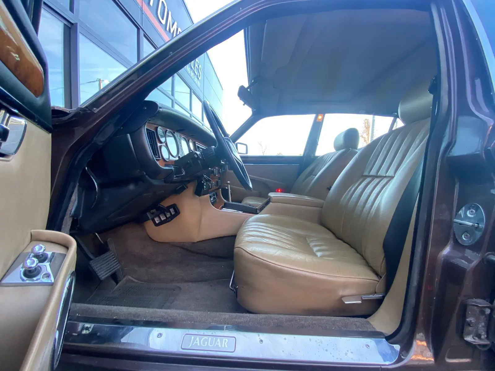 Intérieur beige cuir vu côté conducteur d'une Jaguar XJ6 Série 3 4.2 Sovereign marron de 1985 avec tableau de bord en bois.