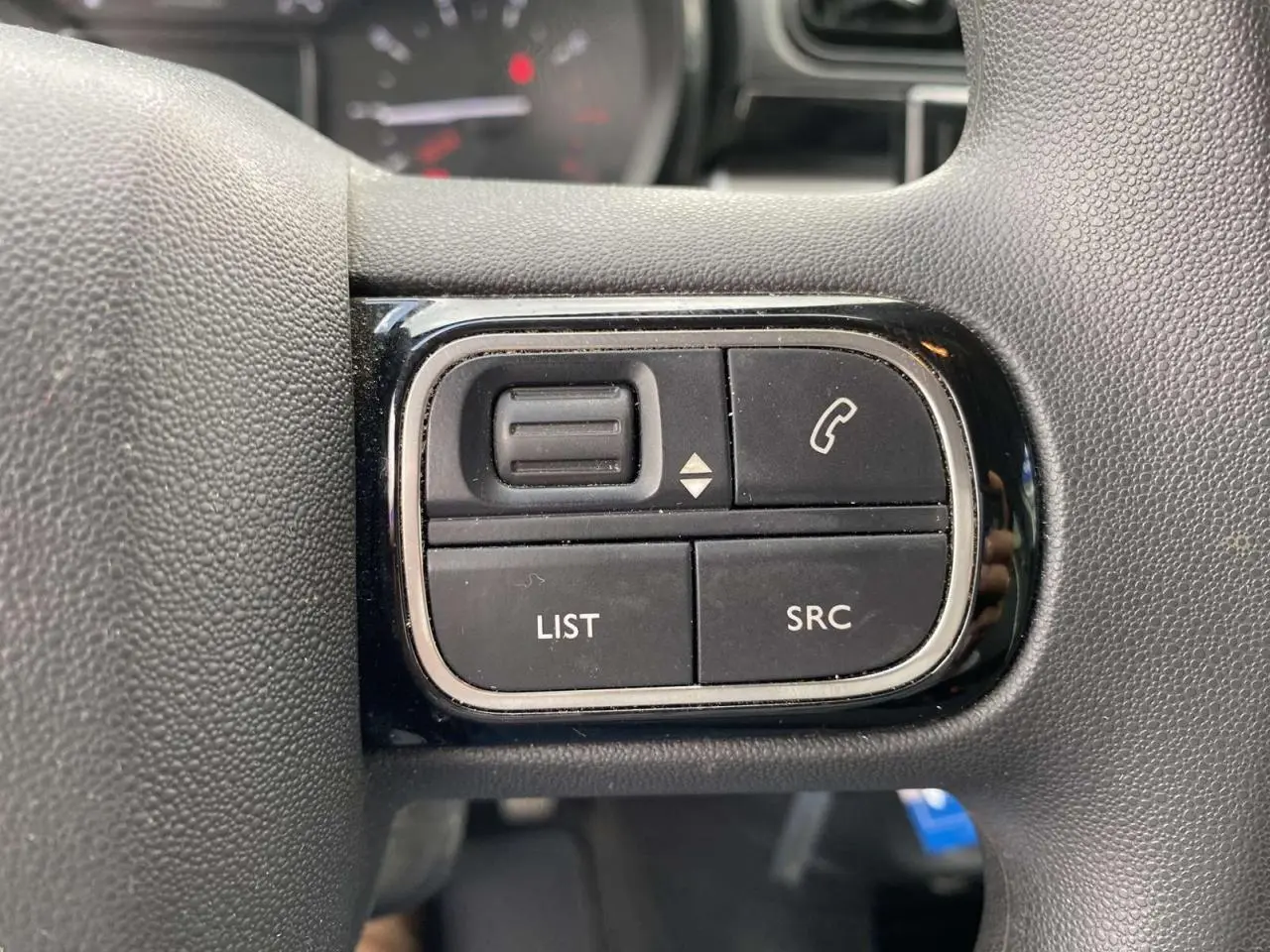 Gros plan sur les commandes multifonctions noires du volant d'une Citroën C3 blanche 2019, version Graphic.