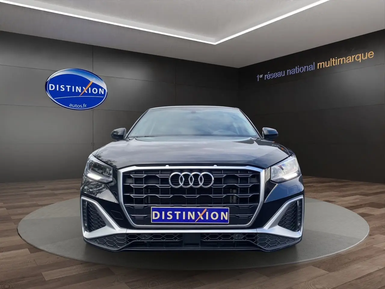Audi Q2 noir mito vue de face dans un showroom avec calandre hexagonale et feux LED allumés.