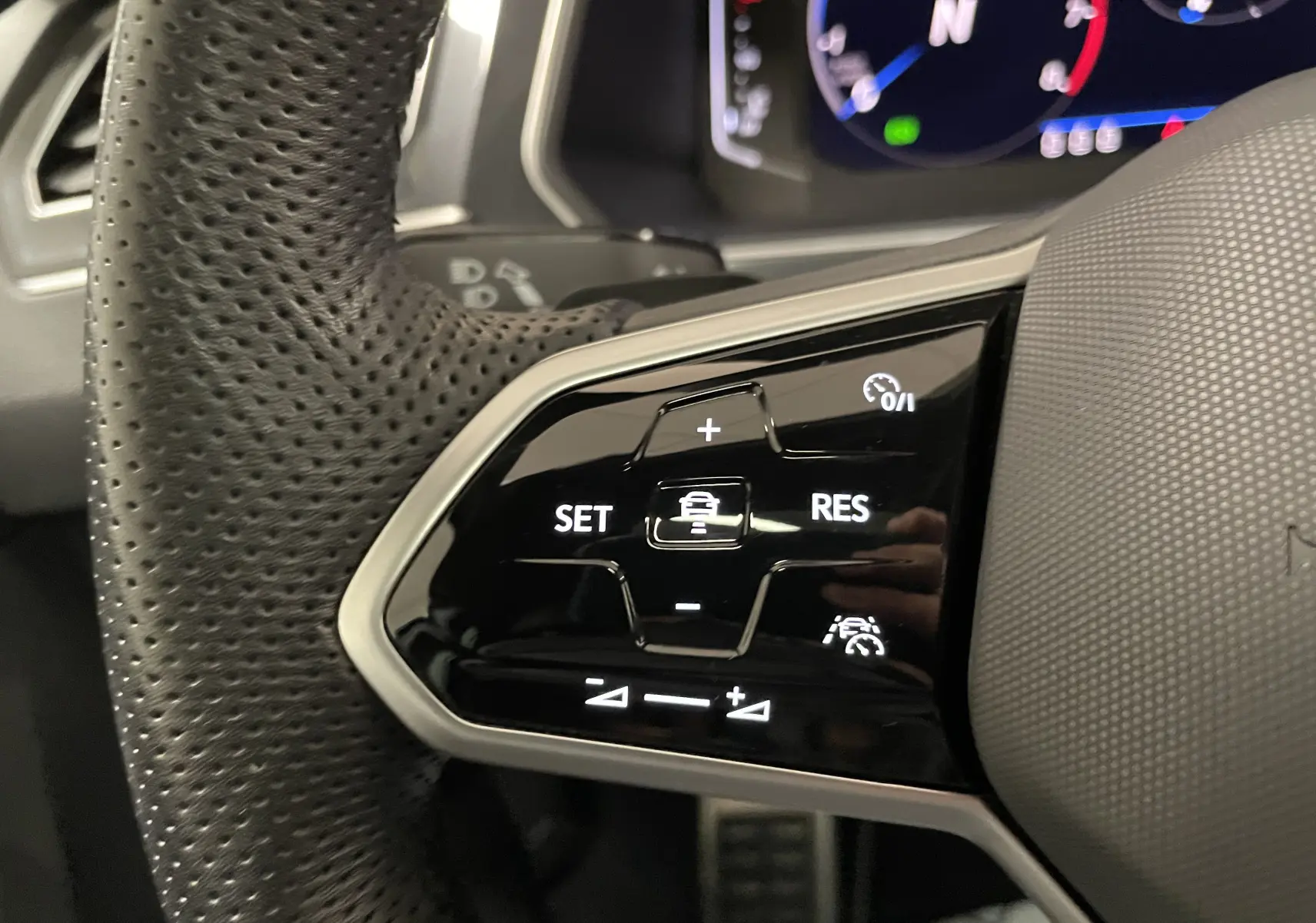 Gros plan sur les commandes au volant perforé du Volkswagen Tiguan 2024, mettant en valeur les fonctions de régulateur de vitesse.