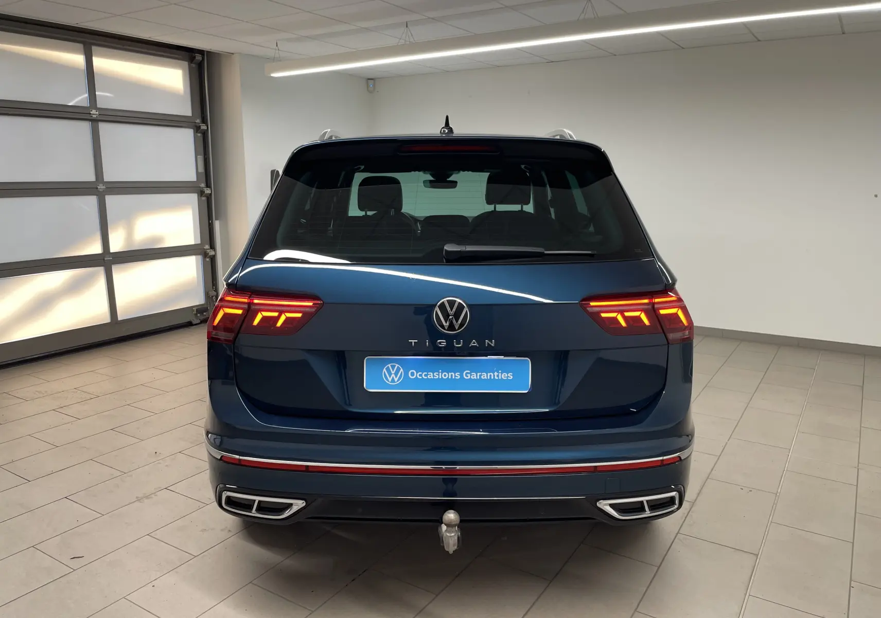 Vue arrière d'un Volkswagen Tiguan 2024 bleu Nightshade avec feux allumés et crochet d'attelage escamotable visible.