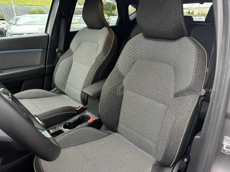 Vue intérieure de face des sièges avant gris du Renault Captur 2025, avec accoudoir central et détails de la porte côté gauche.