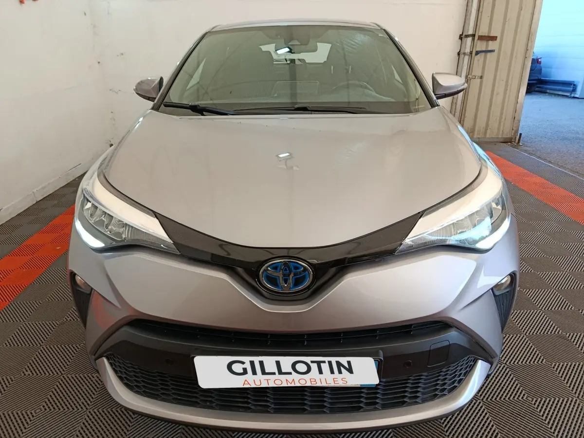 Vue avant d'un Toyota C-HR gris clair 2022 avec phares LED allumés et calandre noire distinctive.