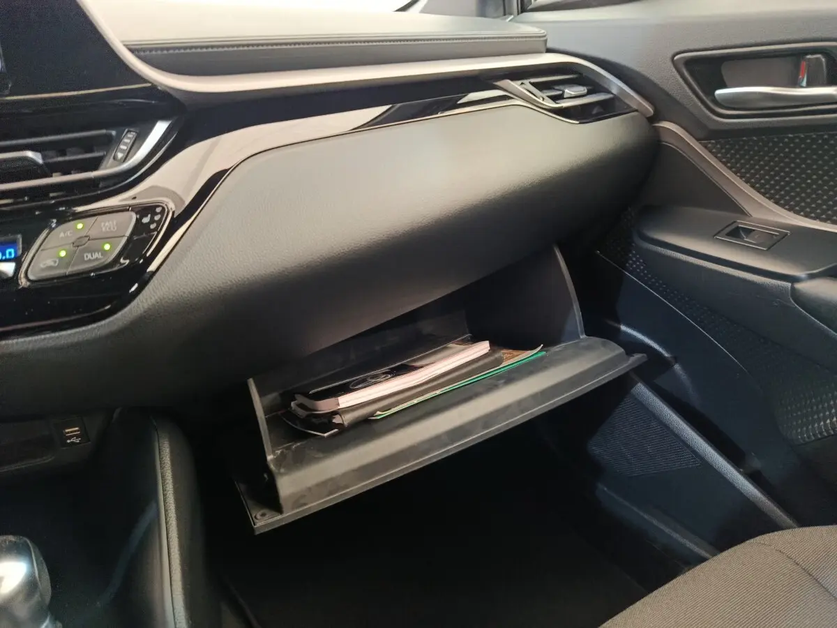 Intérieur du Toyota C-HR 2.0 Hybride 2022, vue côté passager sur la boîte à gants ouverte avec documents visibles.