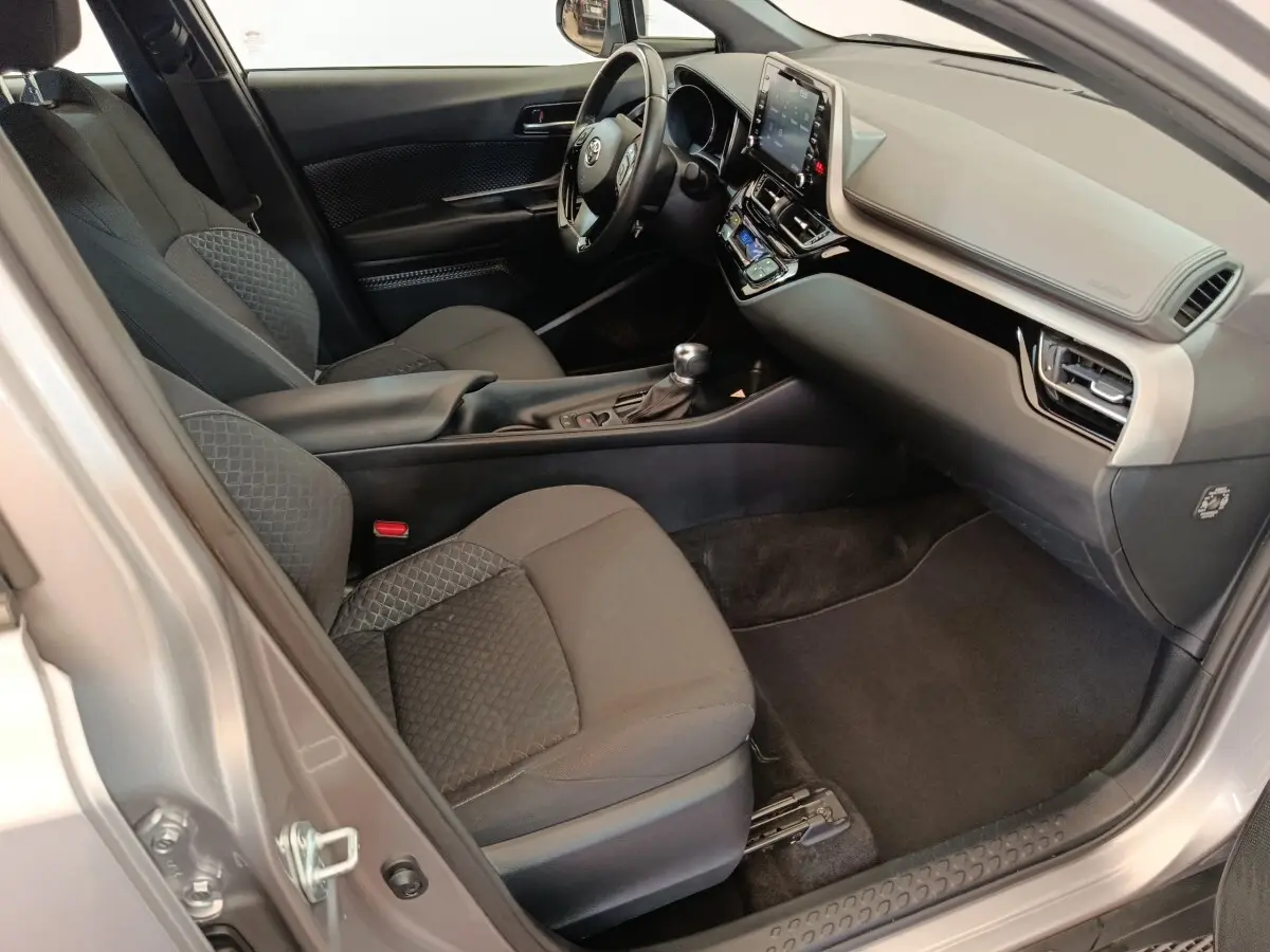 Vue intérieure côté passager du Toyota C-HR gris clair 2022, avec tableau de bord moderne et sièges tissu noirs.