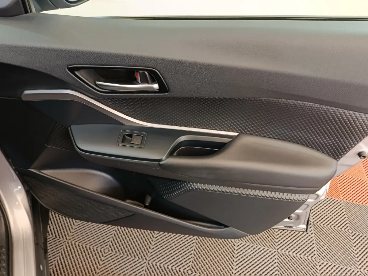 Gros plan sur la porte intérieure côté conducteur du Toyota C-HR gris clair, montrant la poignée et les commandes de fenêtre.