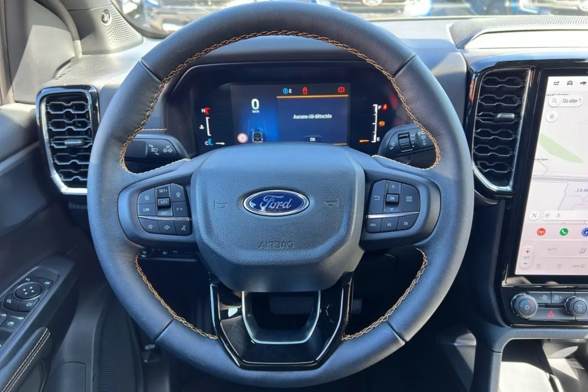 Vue rapprochée du volant en cuir avec surpiqûres marron du Ford Ranger gris carbone 2025, tableau de bord numérique et écran tactile.