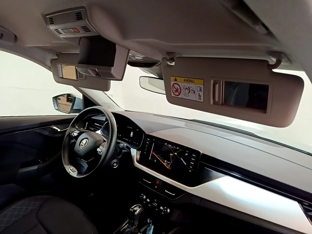 Intérieur du Skoda Kamiq 2022 vu côté conducteur, tableau de bord clair avec écran tactile et volant cuir multifonctions.