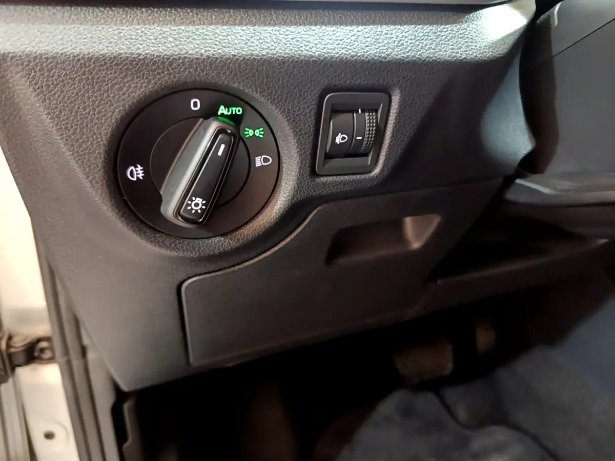 Gros plan sur la commande des phares et réglage de hauteur dans l'habitacle gris foncé d'une Skoda Kamiq 2022.