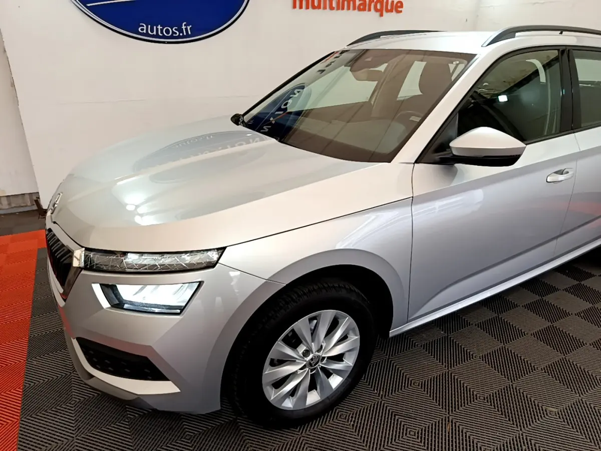 Vue 3/4 avant droit d'un Skoda Kamiq gris clair avec phares LED et jantes alliage en intérieur showroom.