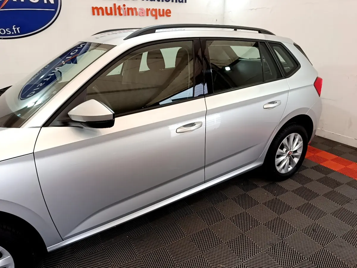 Profil côté gauche d'un Skoda Kamiq gris clair 2022 avec jantes alliage et rétroviseur blanc en intérieur showroom.