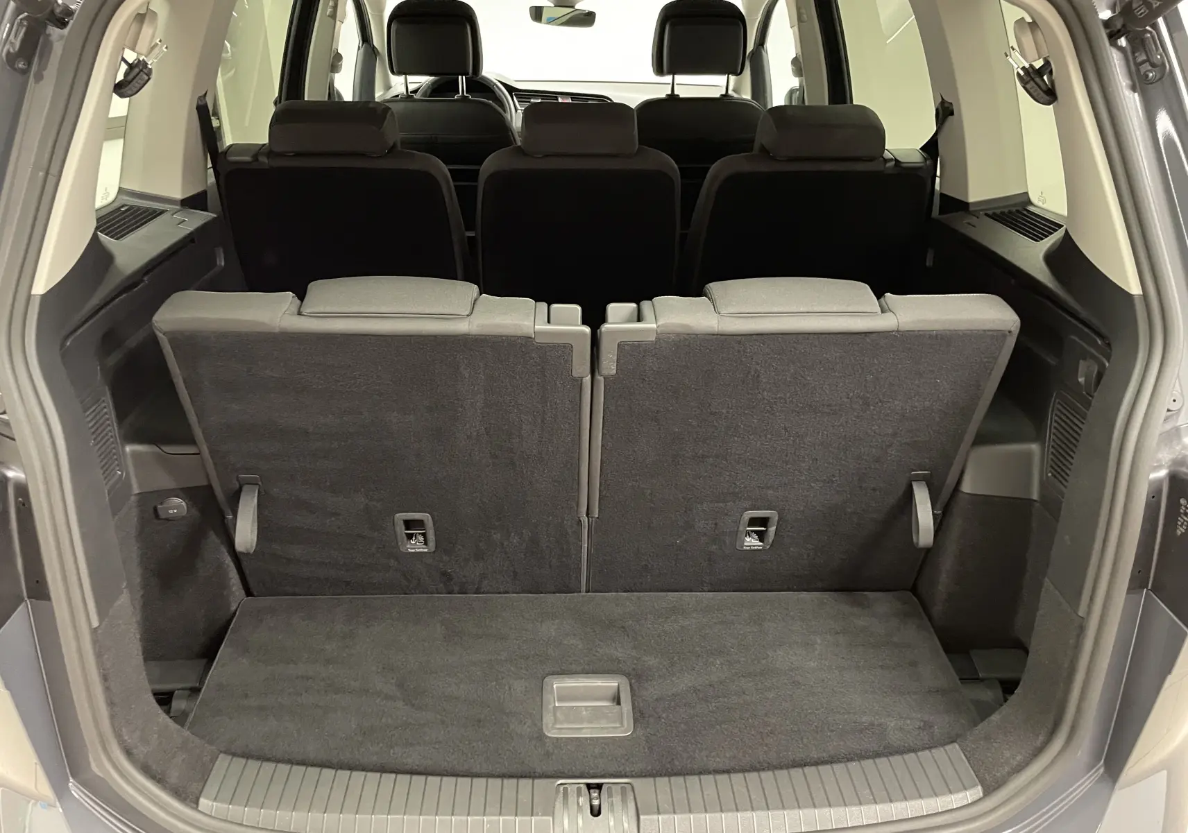 Coffre ouvert d'un Volkswagen Touran gris dauphin 2024, vue arrière montrant la troisième rangée de sièges relevée.