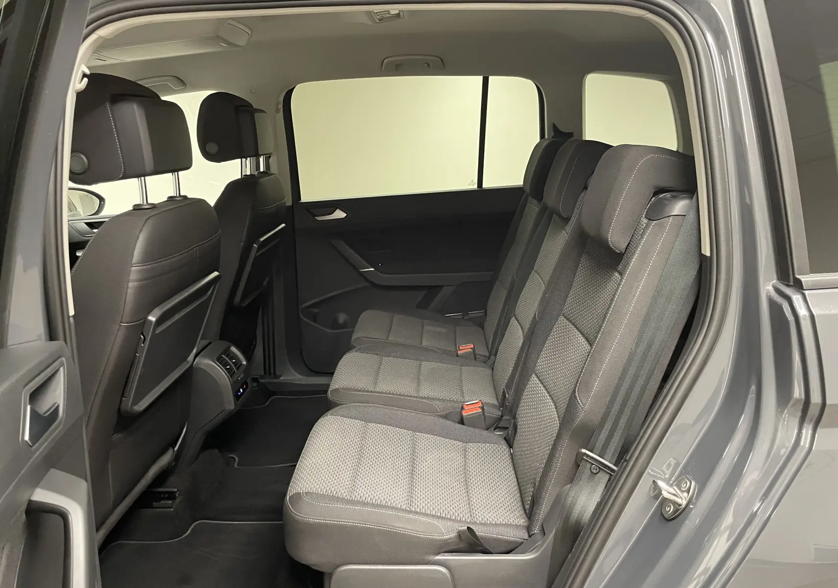 Intérieur arrière du Volkswagen Touran gris Dauphin, vue côté droit sur les trois sièges passagers en tissu gris.