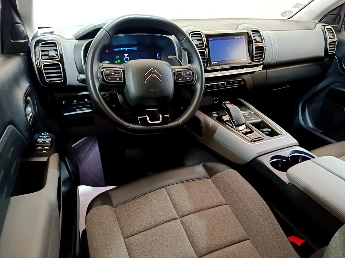 Vue intérieure avant du Citroën C5 Aircross Hybrid gris clair, volant cuir, écran tactile et console centrale moderne.
