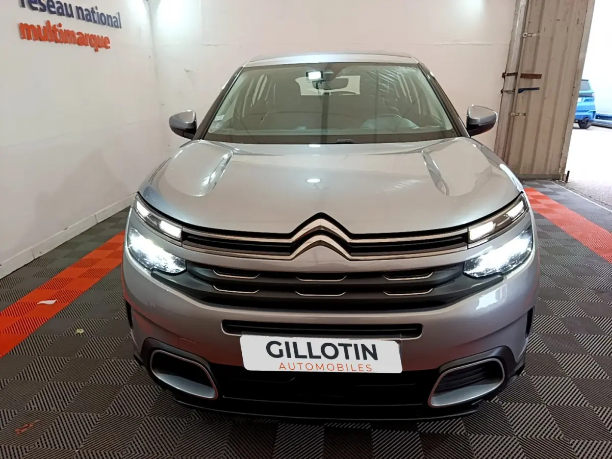 Vue frontale d'un Citroën C5 Aircross gris clair avec phares LED allumés dans un showroom fermé.
