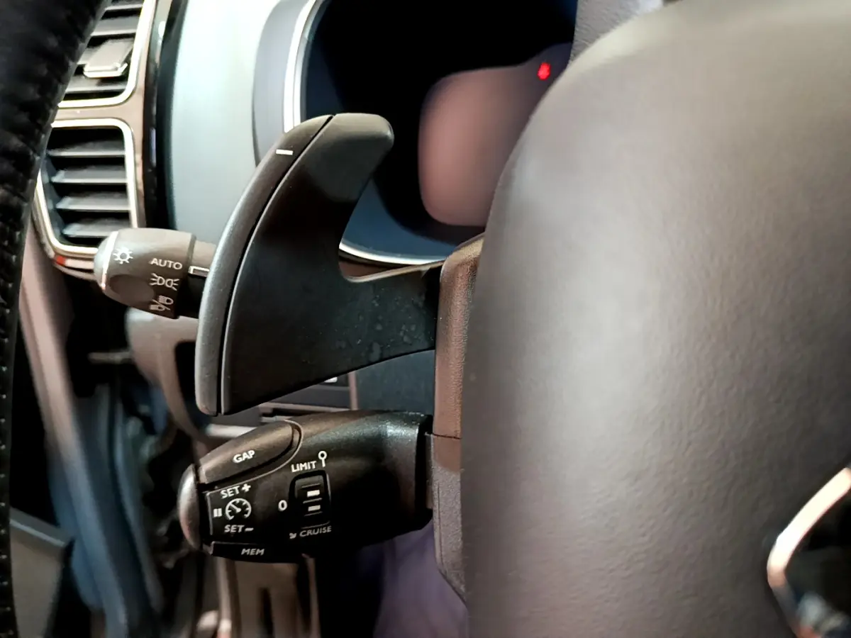 Gros plan sur la commande de régulateur de vitesse à gauche du volant cuir du Citroën C5 Aircross Hybrid 225 gris clair.