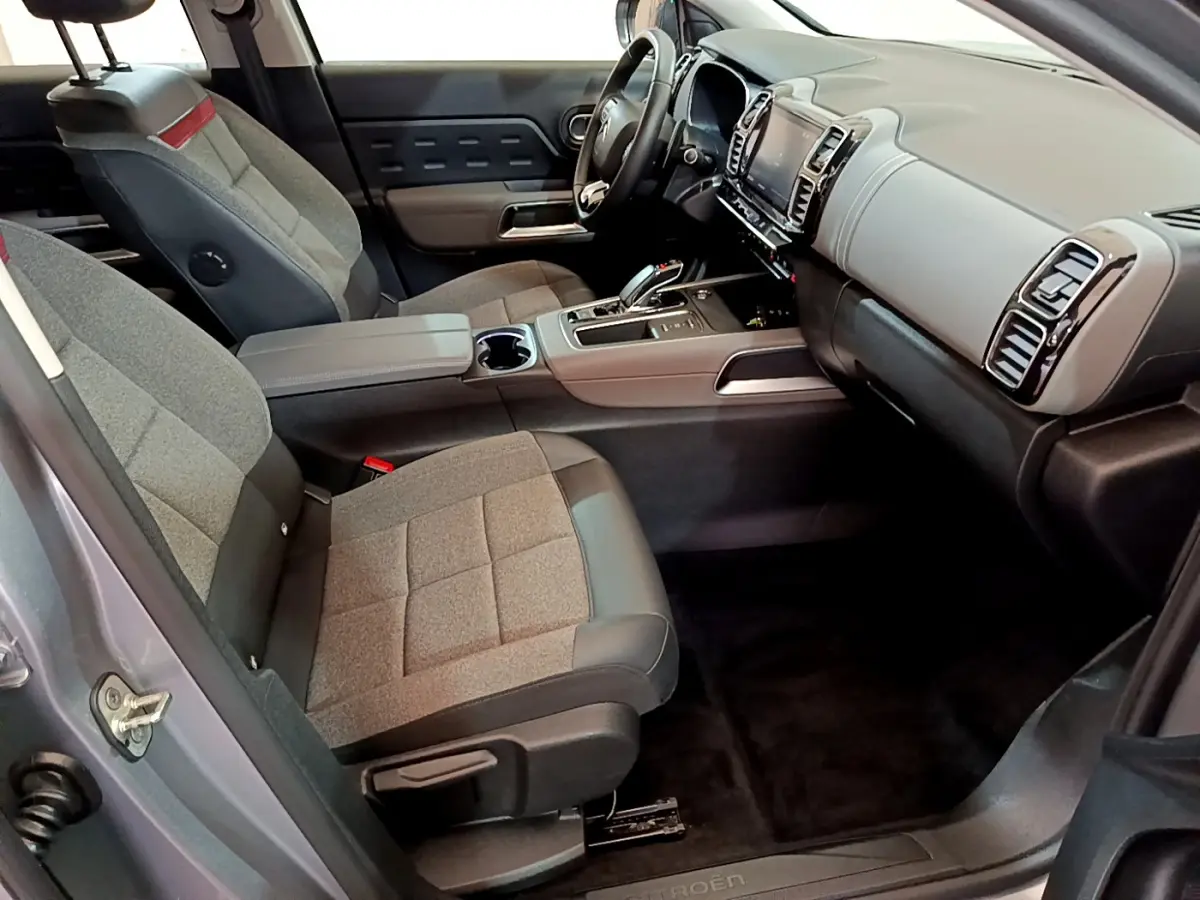 Vue intérieure côté conducteur de la Citroën C5 Aircross Hybrid gris clair, avec tableau de bord moderne et sièges tissu gris.