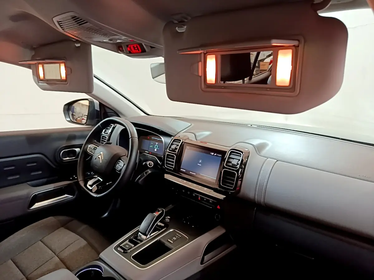 Intérieur du Citroën C5 Aircross Hybrid gris clair vu côté conducteur, tableau de bord et écran tactile éclairés.