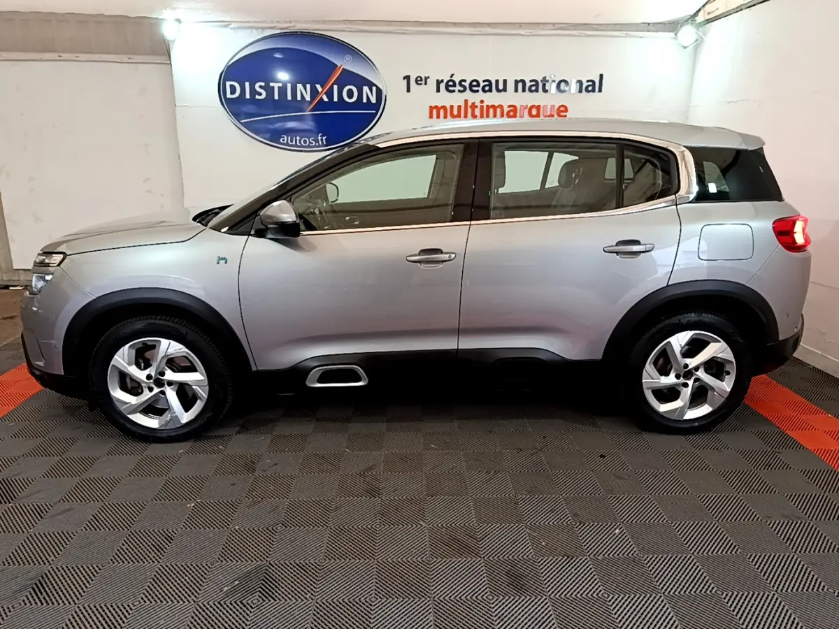 Profil côté gauche d'un Citroën C5 Aircross Hybrid gris clair en intérieur avec jantes alliage et logo hybride visible.