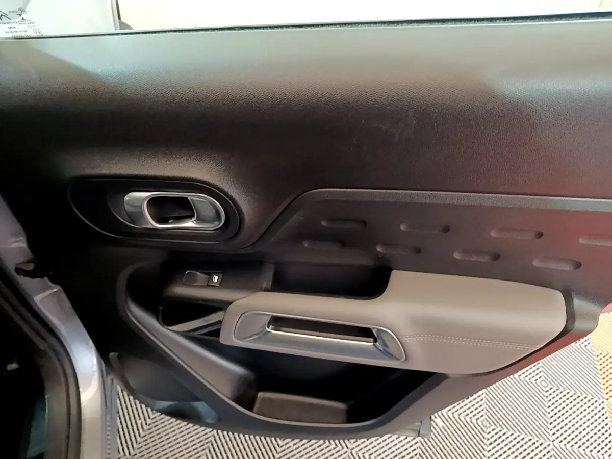 Vue rapprochée de la porte côté gauche du Citroën C5 Aircross Hybrid gris clair, avec poignée intérieure chromée et accoudoir beige.