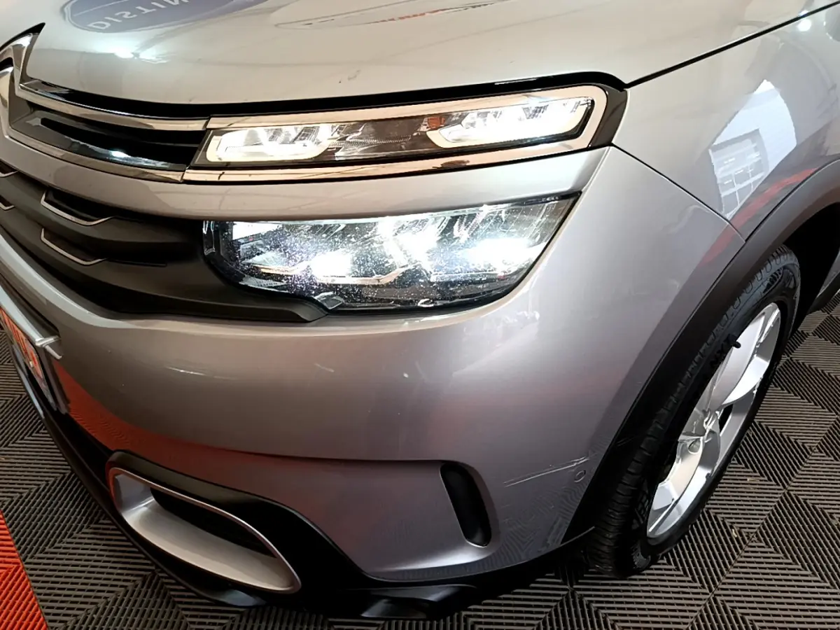 Gros plan sur l'avant droit gris clair du Citroën C5 Aircross Hybrid 225 avec phares LED allumés et jante visible.