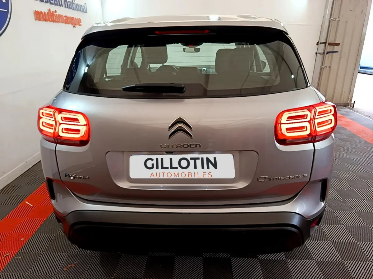 Vue arrière d'un Citroën C5 Aircross Hybrid gris clair avec feux arrière LED allumés en intérieur showroom.
