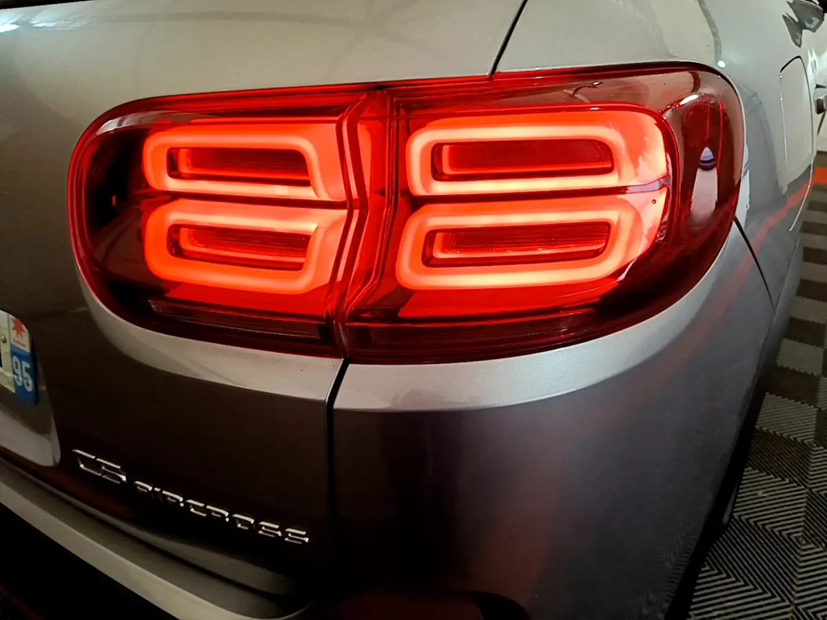 Feu arrière droit allumé sur Citroën C5 Aircross gris clair, détail du logo et de la carrosserie arrière.
