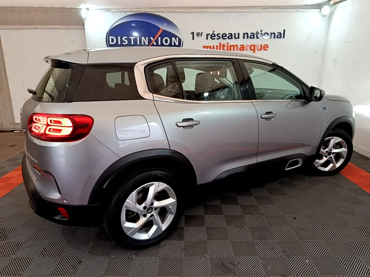 Vue 3/4 arrière droite d'un Citroën C5 Aircross Hybrid gris clair avec feux arrière LED allumés en intérieur showroom.