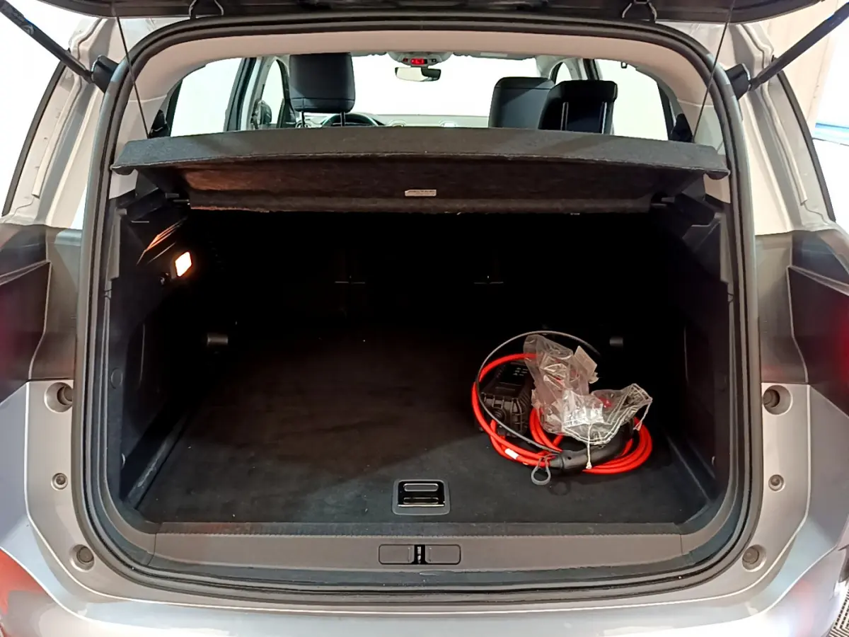 Coffre ouvert vu de l'arrière d'un Citroën C5 Aircross gris clair avec câble de recharge hybride visible à droite.