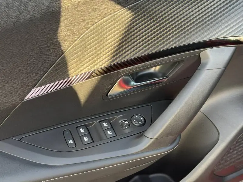 Détail de la porte avant gauche du Peugeot 2008 rouge Elixir, avec insert décoratif effet carbone et commandes des vitres.