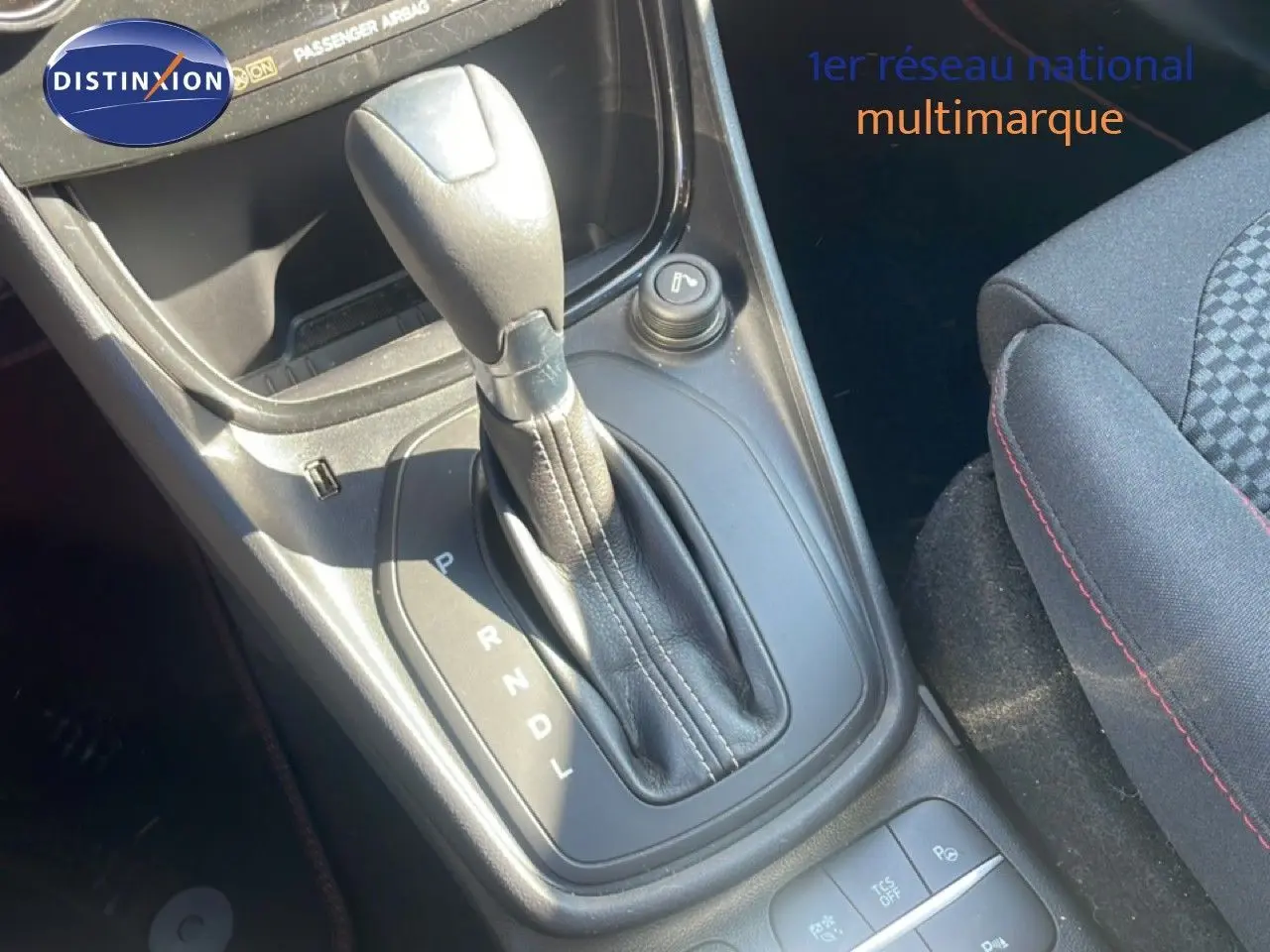 Gros plan sur la console centrale du Ford Puma 2023 avec levier de boîte automatique et siège tissu gris à surpiqûres rouges.