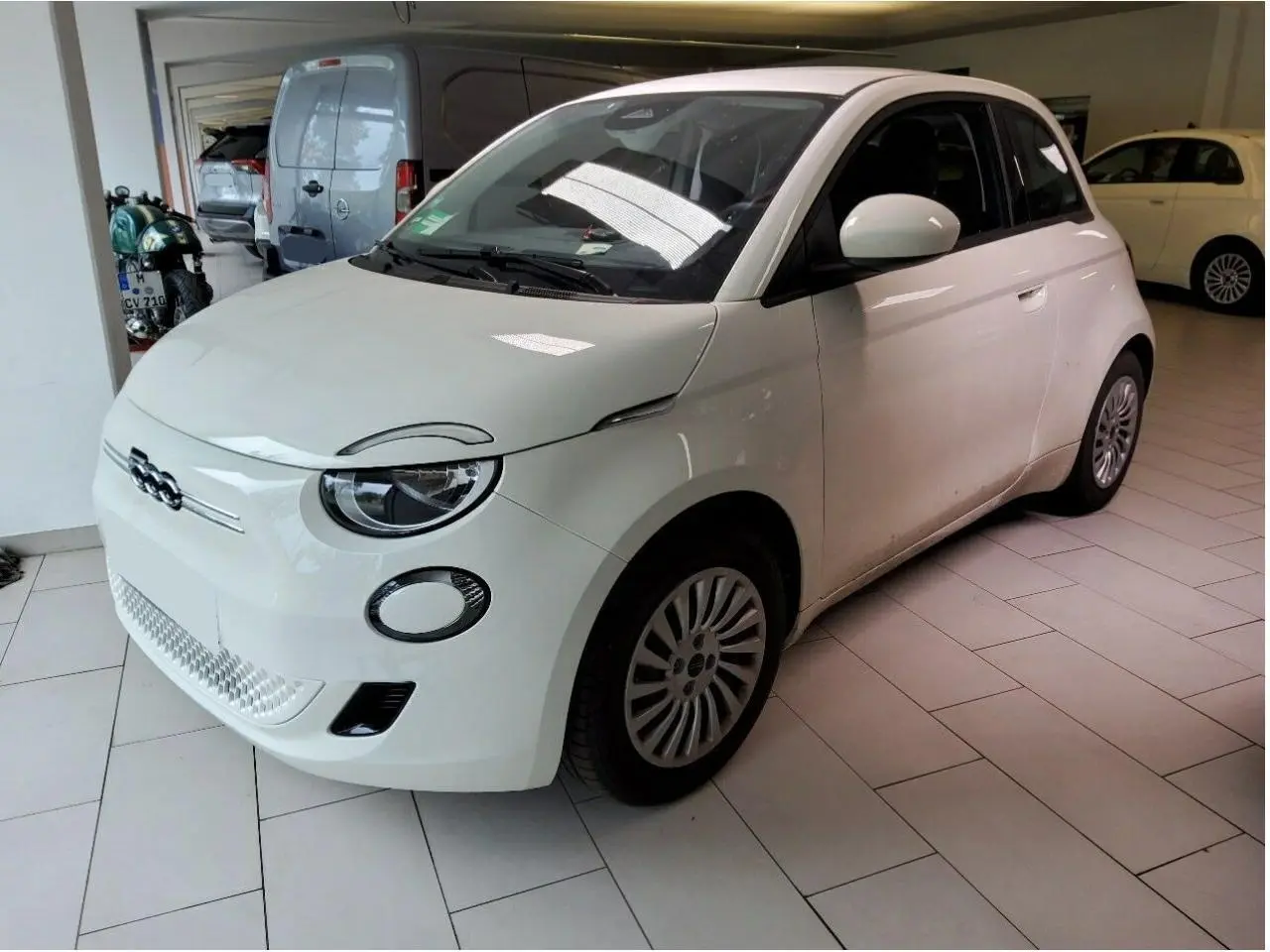 Vue 3/4 avant droite d'une Fiat 500 électrique blanche 2024 avec logo distinctif et jantes multibranches.