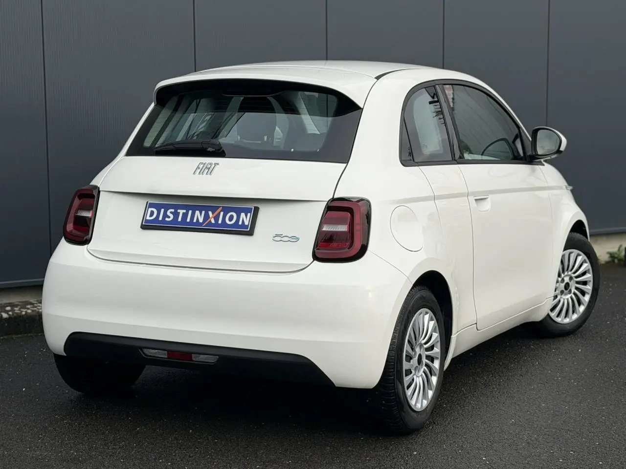 Vue 3/4 arrière droite d'une Fiat 500 électrique blanche avec feux arrière sombres et jantes multibranches.