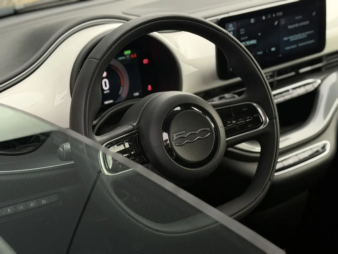 Vue rapprochée du volant noir et du tableau de bord blanc de la Fiat 500 électrique 2024 avec écran digital.