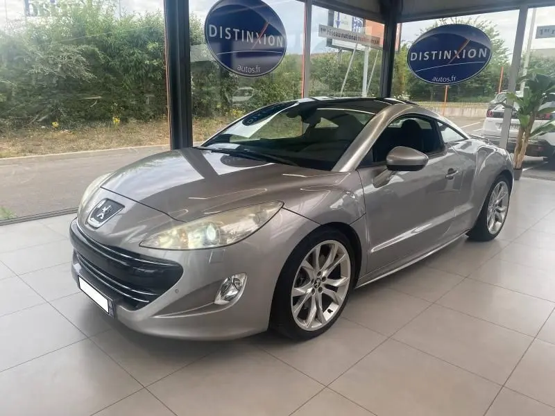 Peugeot RCZ gris en 3/4 avant droit, avec jantes alliage et toit panoramique visible en showroom.