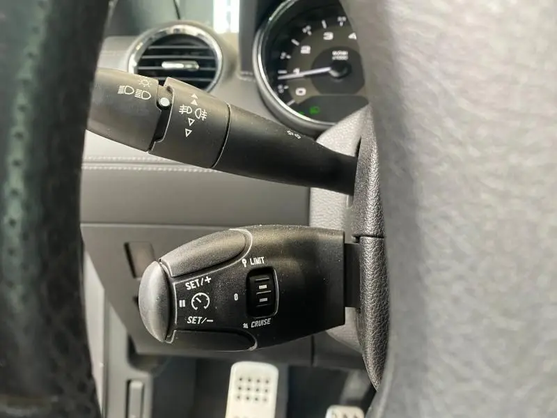 Gros plan sur les commandes au volant du Peugeot RCZ gris 2010, mettant en valeur les réglages du régulateur de vitesse et des phares.