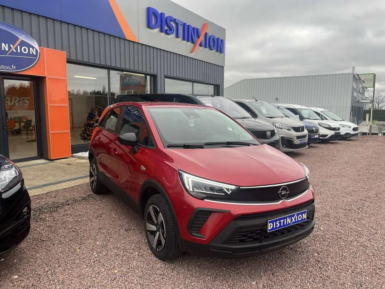 Opel Crossland rouge métallisé en 3/4 avant droit, avec feux LED et calandre noire, stationné devant un concessionnaire.