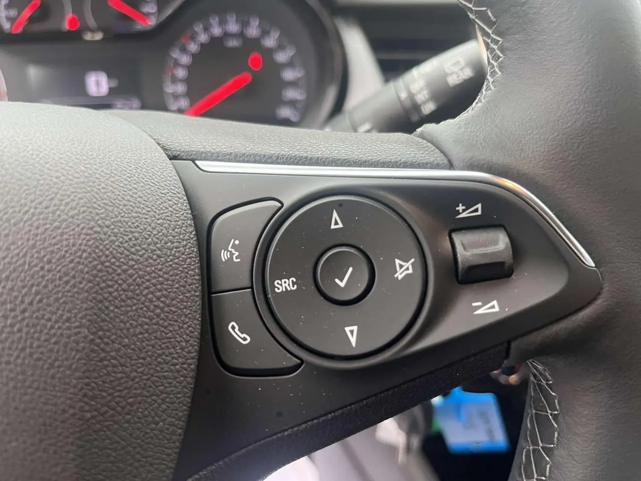 Gros plan sur les commandes au volant noir de l'Opel Crossland rouge, avec boutons de volume et appels téléphoniques.