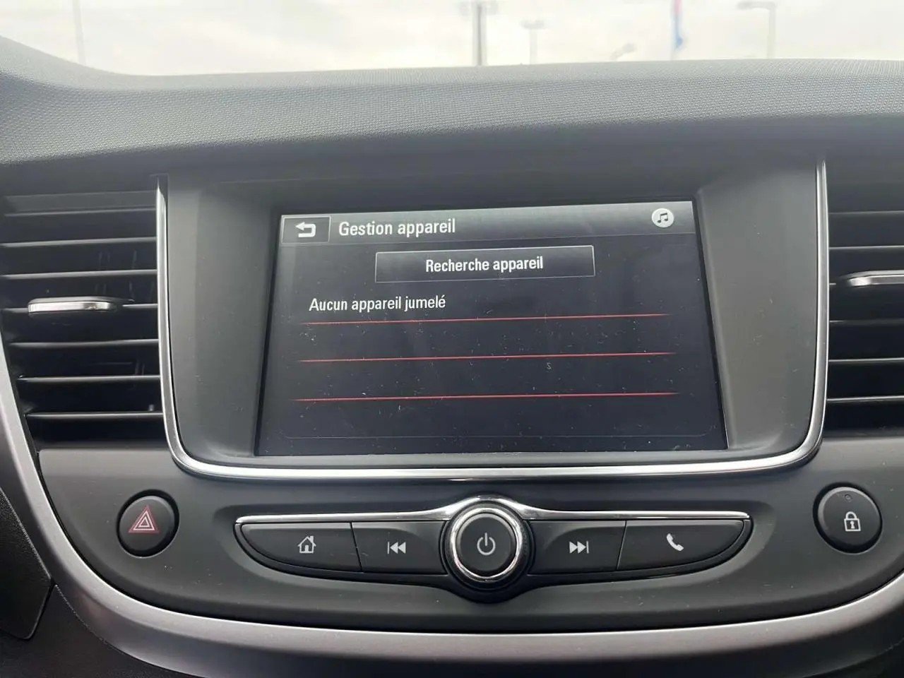 Écran tactile central de l’Opel Crossland rouge 2022 affichant la gestion des appareils Bluetooth, boutons de commande en dessous.